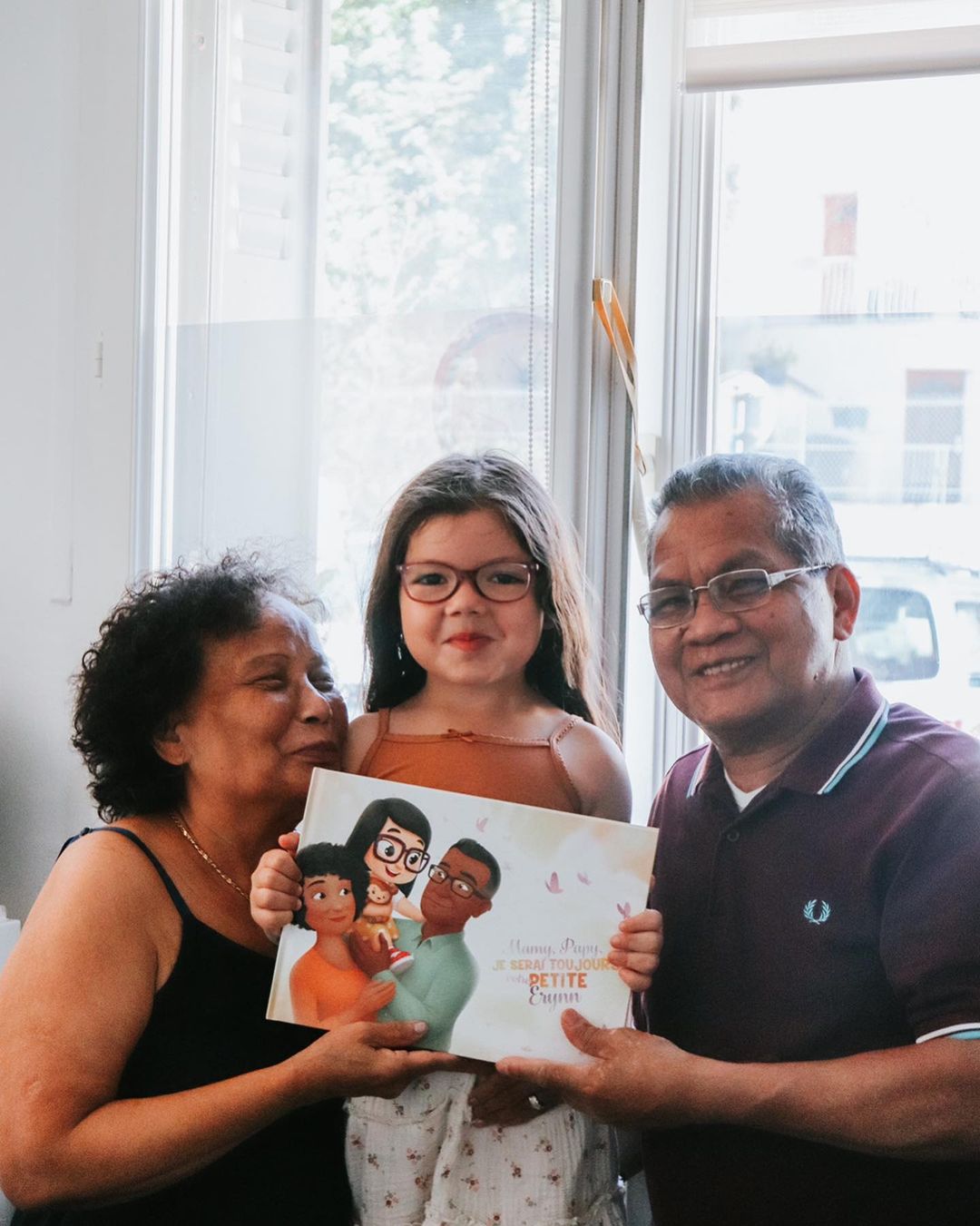 Une petite fille entourée par ses grands parents après avoir offert un livre personnalisé pour la fête des grands-parents.