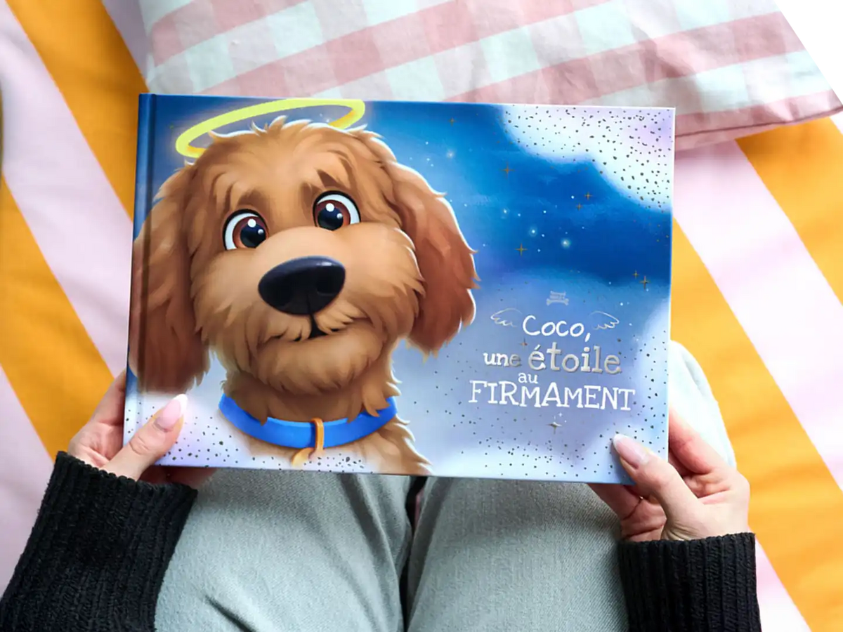 Personne tenant un livre mémoire personnalisé pour chien intitulé « Coco, une étoile au firmament ».