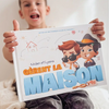 Un petit garçon tenant un livre personnalisé seul à la maison pour ses frères et sœurs.