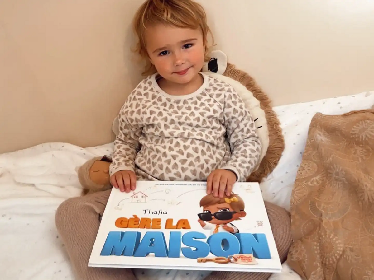 Une petite fille tenant son nouveau livre personnalisé sur le fait d'être seule à la maison.