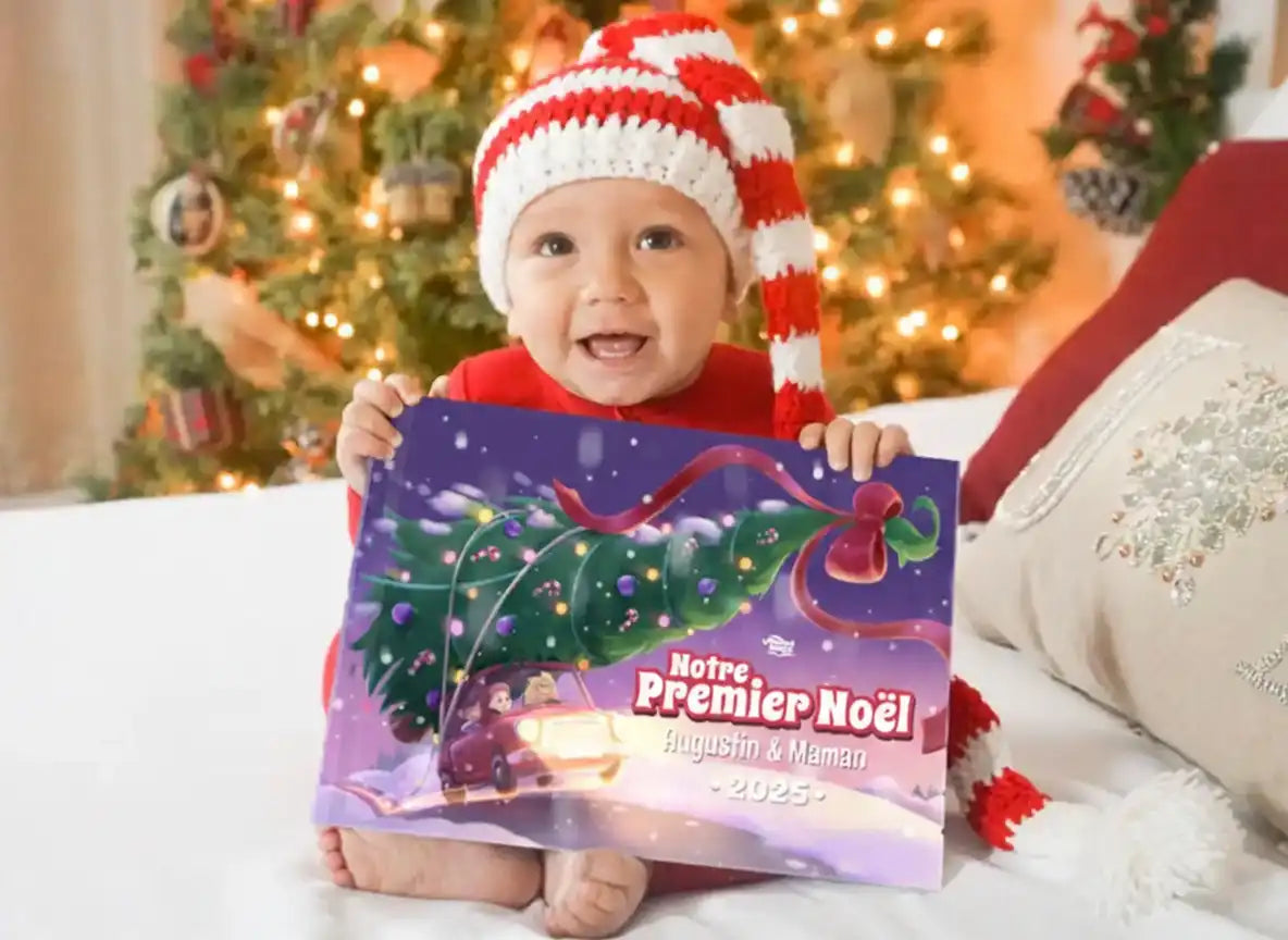 Bébé souriant en bonnet de Noël tenant le livre personnalisé “Notre Premier Noël 2025” avec Augustin et Maman.