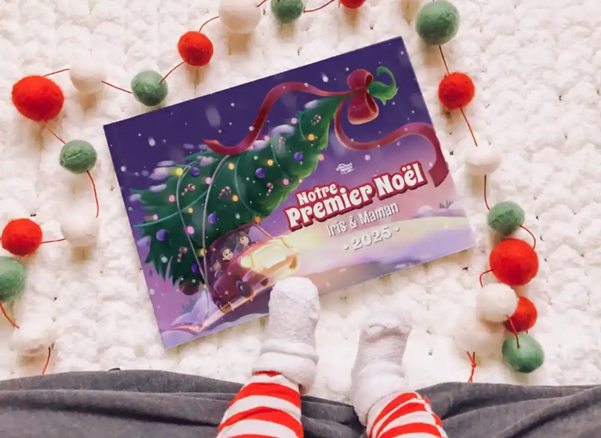 Livre de Noël personnalisé “Notre Premier Noël 2025” avec Iris et Maman, posé à côté des pieds d’un bébé en pyjama rayé.